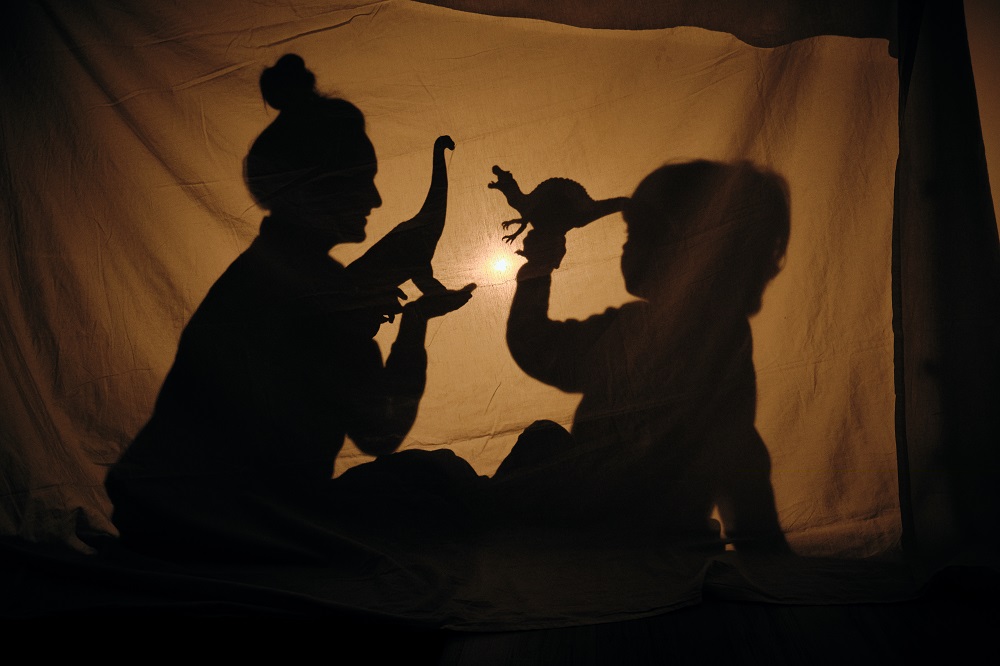 Qué es el storytelling: mamá y niño cuentan historia detrás de una sábana, siluetas.